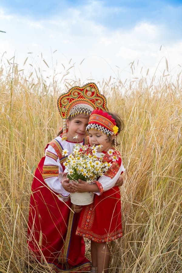 Two girls in the Russian national sundresses and kokoshniks about wheat field with a bouquet of camomiles. Two girls in the Russian national sundresses and kokoshniks about wheat field with a bouquet of camomiles