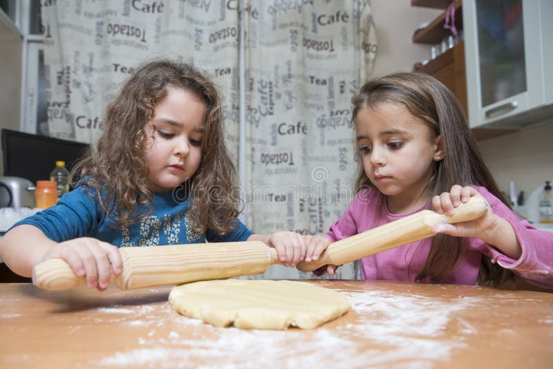 Deux filles déroulant la pâte sur la table de cuisine photographie stock libre de droits Deux filles déroulant la pâte sur la table de cuisine photographie stock libre de droits