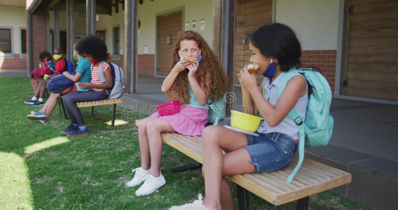 Deux filles manger le déjeuner de la zone tiffin tous assis sur le banc dans le parc à l'école banque de vidéos