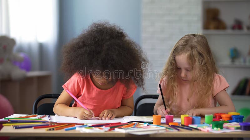 Two multi-racial girls drawing with colorful pencils in early education center, stock photo. Two multi-racial girls drawing with colorful pencils in early education center, stock photo