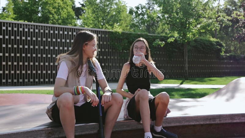 Deux filles se détendre et boire de l'eau douce d'une bouteille en plastique après une séance d'entraînement active sur un skatebo clips vidéos