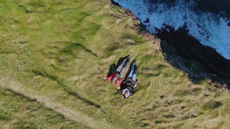 Deux filles se situant dans l'herbe aux falaises de la côte irlandaise - vue de bourdon d'en haut