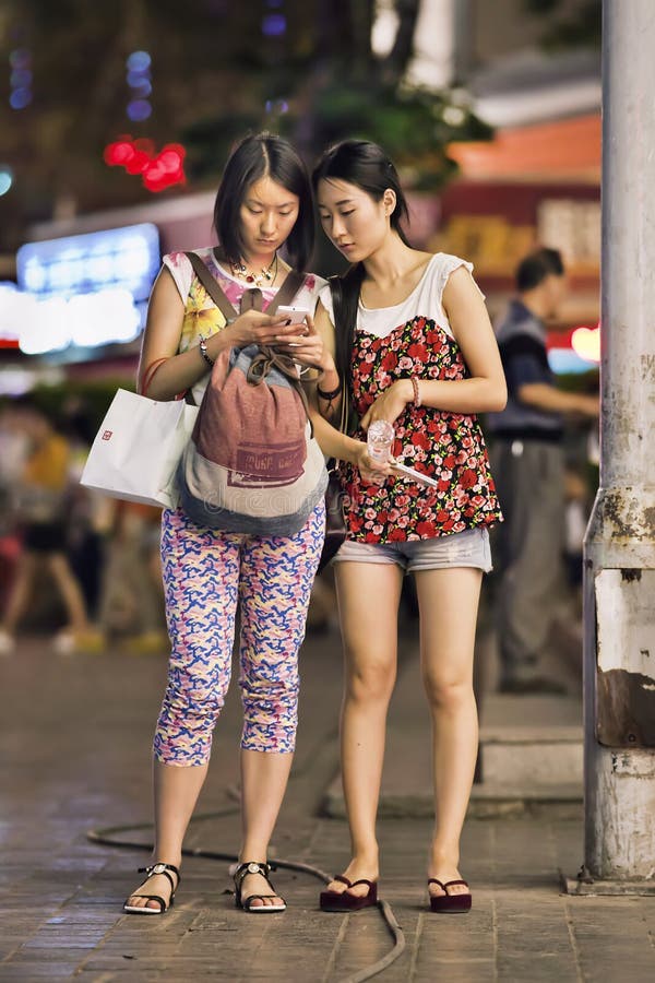 Deux filles à la mode occupées avec le téléphone intelligent dans le centre-ville, Kunming, Chine