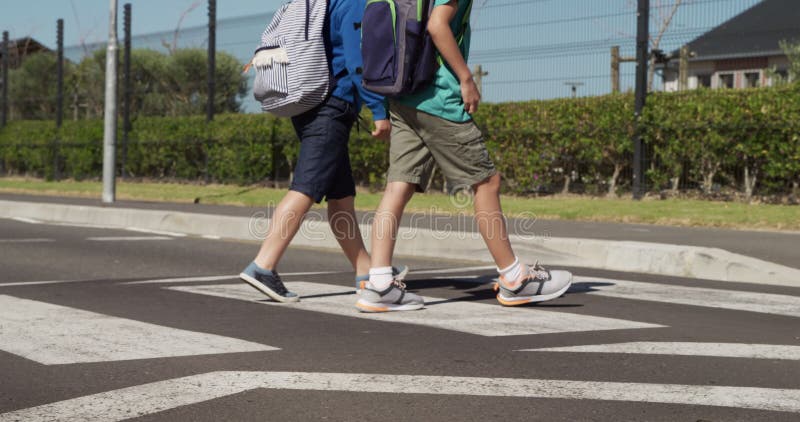 Deux garçons avec des sacs d'école traversant la route banque de vidéos