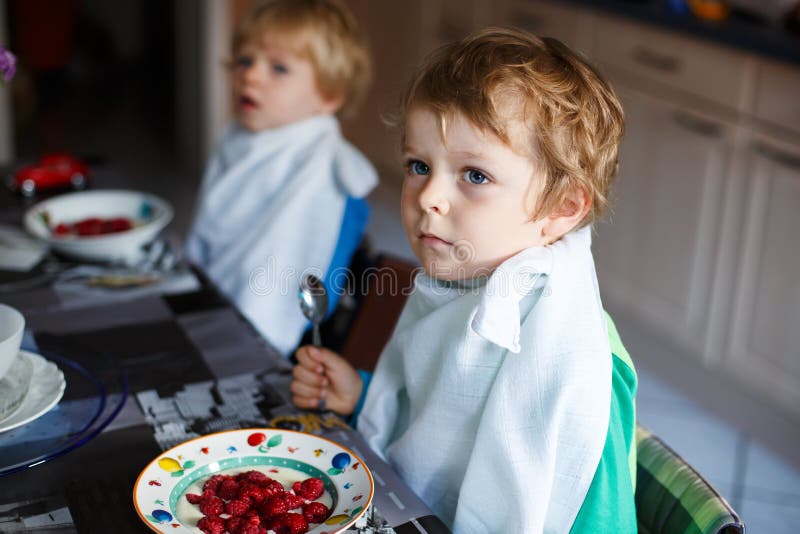Deux garçons de petit frère ayant l'avoine et les baies pour le petit déjeuner images libres de droits Deux garçons de petit frère ayant l'avoine et les baies pour le petit déjeuner images libres de droits