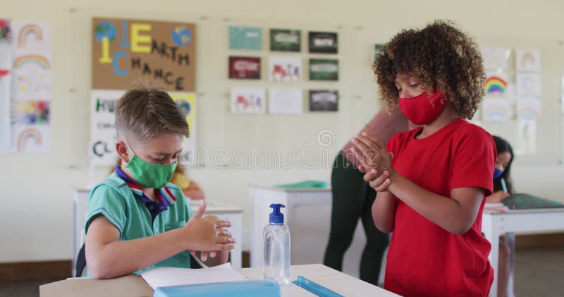 Deux garçons portant des masques de protection de désinfection de leurs mains dans la classe à l'école clips vidéos