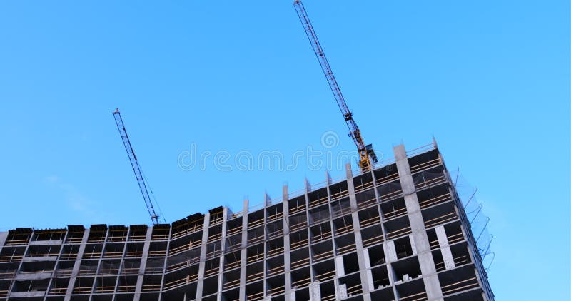 Deux grues de construction s'élèvent sur un bâtiment de plusieurs étages sous des fenêtres de construction en béton qui n'ont pas banque de vidéos
