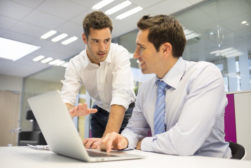 Deux hommes d'affaires beaux travaillant ensemble sur un ordinateur portable dans image stock Deux hommes d'affaires beaux travaillant ensemble sur un ordinateur portable dans image stock