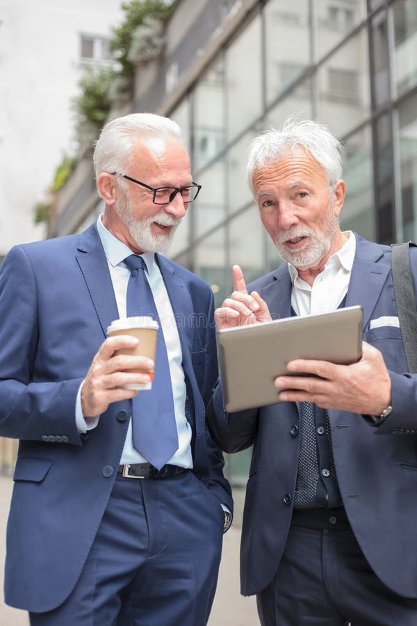 Deux hommes d'affaires d'une chevelure gris supérieurs parlant devant un immeuble de bureaux photographie stock Deux hommes d'affaires d'une chevelure gris supérieurs parlant devant un immeuble de bureaux photographie stock