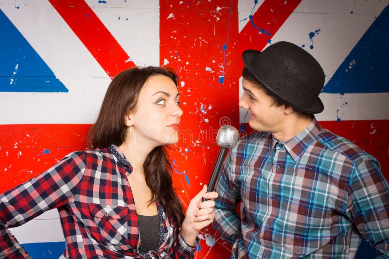 Two performers doing a British comedy show standing in front of a Union Jack painted on a wall using a microphone wearing patriotic clothing and a bowler hat. Two performers doing a British comedy show standing in front of a Union Jack painted on a wall using a microphone wearing patriotic clothing and a bowler hat