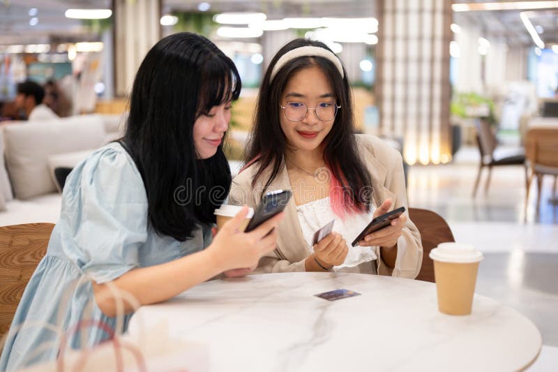 Two happy young Asian female friends are hanging out together at the shopping mall on the weekend, talking about something on their phones while sitting in a cafe. lifestyle concept. Two happy young Asian female friends are hanging out together at the shopping mall on the weekend, talking about something on their phones while sitting in a cafe. lifestyle concept