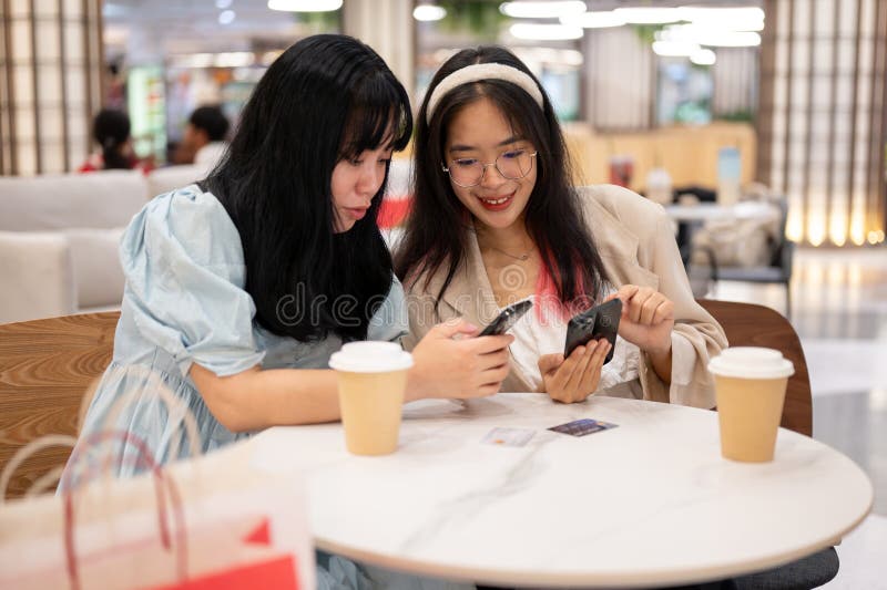 Two happy young Asian female friends are hanging out together at the shopping mall on the weekend, talking about something on their phones while sitting in a cafe. lifestyle concept. Two happy young Asian female friends are hanging out together at the shopping mall on the weekend, talking about something on their phones while sitting in a cafe. lifestyle concept