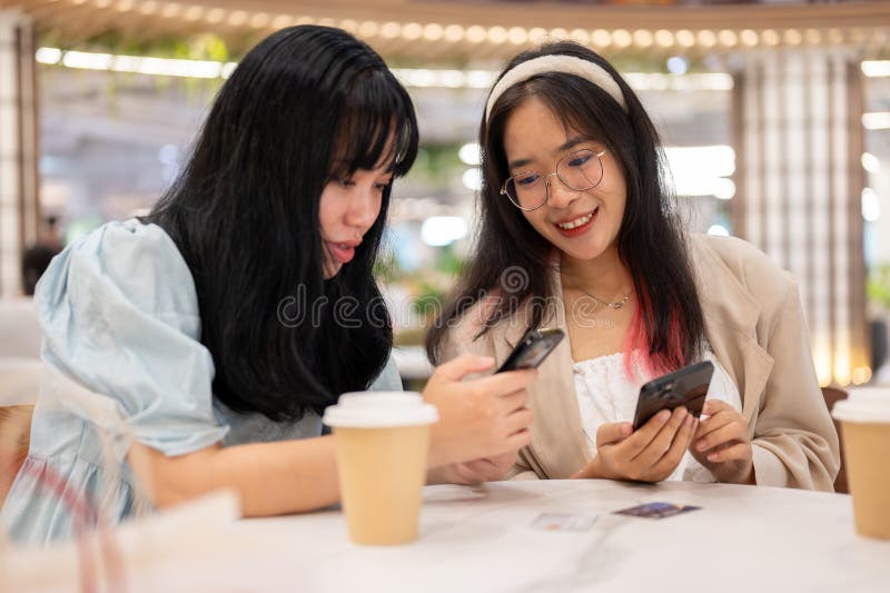 Two happy young Asian female friends are hanging out together at the shopping mall on the weekend, talking about something on their phones while sitting in a cafe. lifestyle concept. Two happy young Asian female friends are hanging out together at the shopping mall on the weekend, talking about something on their phones while sitting in a cafe. lifestyle concept