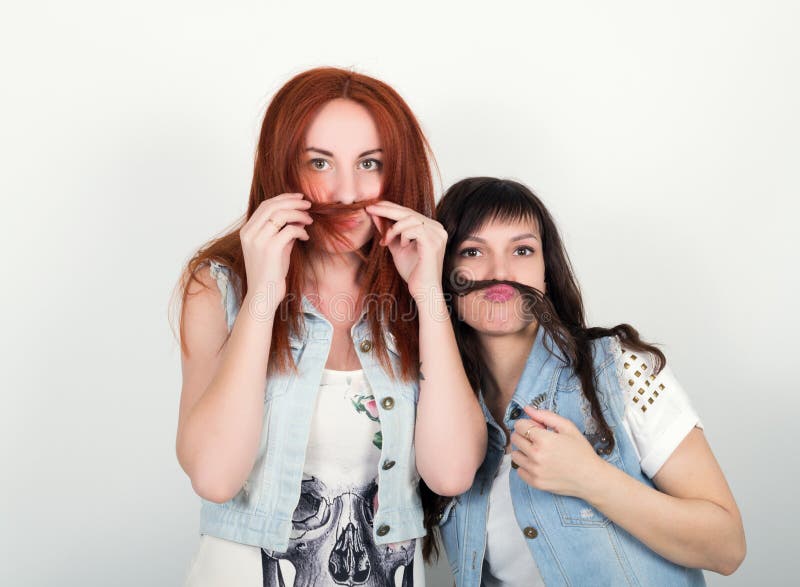 Deux jeunes amies se livrent et grimacent, se fabriquent une moustache à partir de les cheveux Adolescent faisant la moustache à photographie stock libre de droits Deux jeunes amies se livrent et grimacent, se fabriquent une moustache à partir de les cheveux Adolescent faisant la moustache à photographie stock libre de droits
