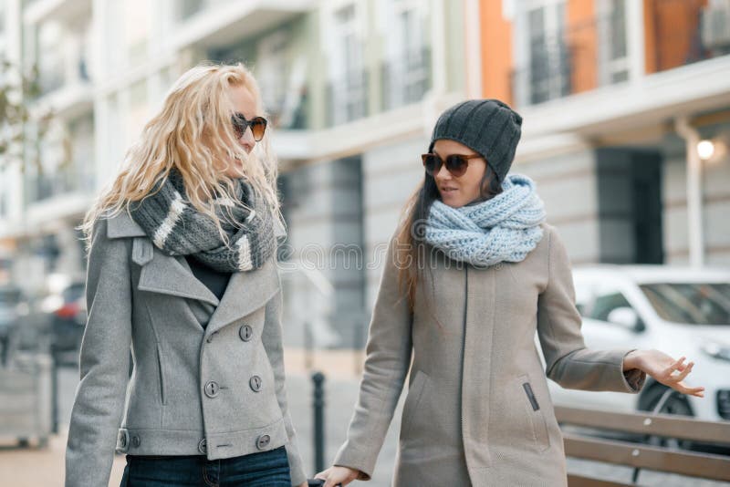 Deux jeunes belles femmes de sourire dans des vêtements chauds descendant la rue de ville avec une valise de voyage, femmes riant image stock Deux jeunes belles femmes de sourire dans des vêtements chauds descendant la rue de ville avec une valise de voyage, femmes riant image stock