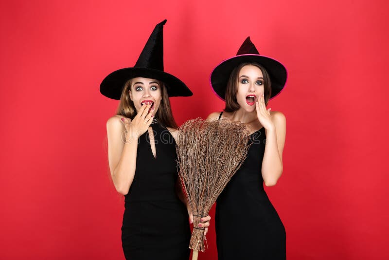 Two young women in black halloween costumes with broom on red background. Two young women in black halloween costumes with broom on red background