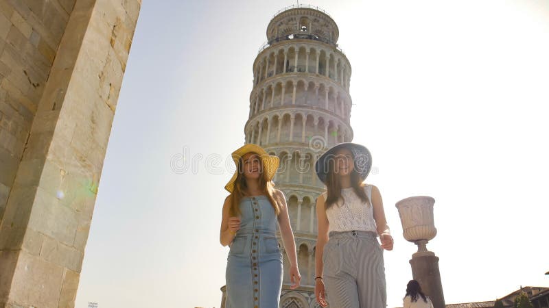 Deux jeunes femmes de sourire se tenant sur un fond de la tour penchée photo stock Deux jeunes femmes de sourire se tenant sur un fond de la tour penchée photo stock