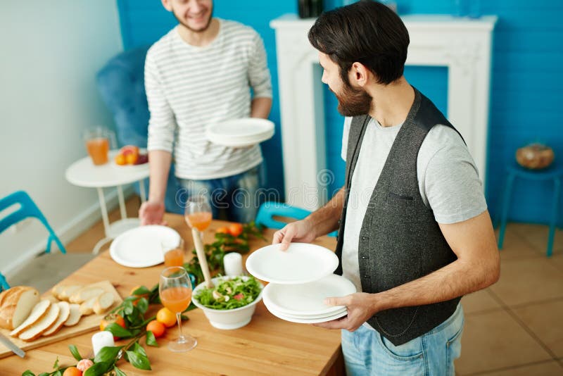 Deux jeunes hommes mettant la table pour la collecte d'amis images stock Deux jeunes hommes mettant la table pour la collecte d'amis images stock