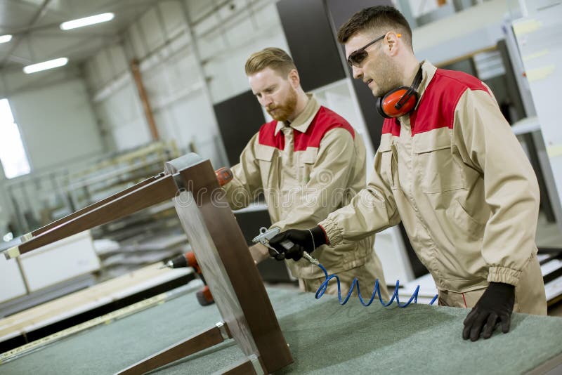 Deux jeunes travailleurs assemblant des meubles dans l'usine photo libre de droits Deux jeunes travailleurs assemblant des meubles dans l'usine photo libre de droits