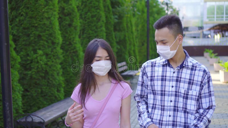 Deux jeunes étudiants asiatiques portant un masque médical sur le visage marchant dans la rue et parlant de près