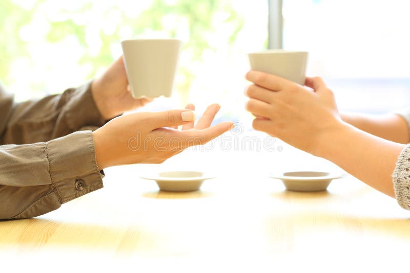 Side view close up of two women hands talking in a bar or house holding coffee cups. Side view close up of two women hands talking in a bar or house holding coffee cups