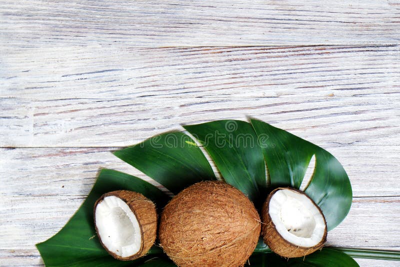 deux moiti?s de noix de coco et d'une noix de coco enti?re avec une feuille d'usine tropicale de monstera sur un fond en bois bla images libres de droits deux moiti?s de noix de coco et d'une noix de coco enti?re avec une feuille d'usine tropicale de monstera sur un fond en bois bla images libres de droits