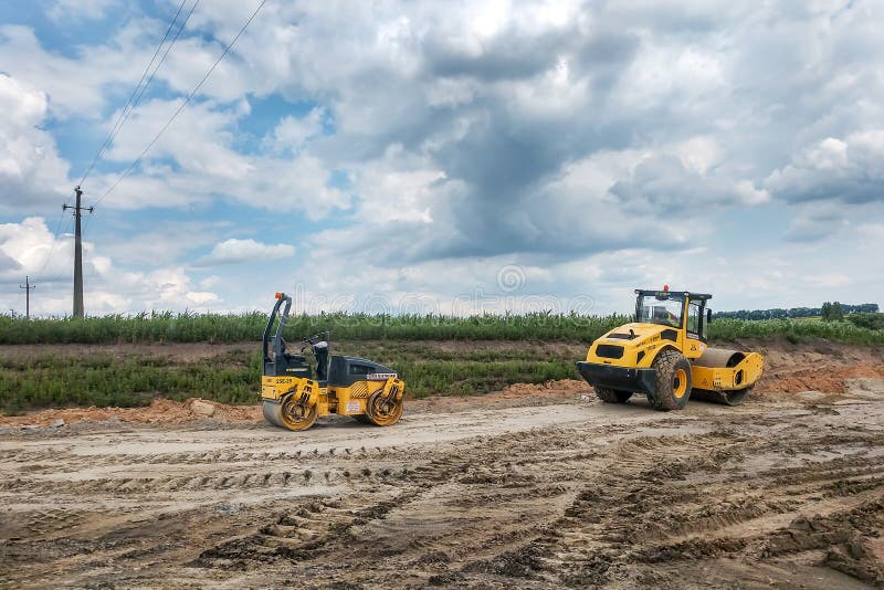 Deux noirs et rouleaux jaunes d'asphalte de route se tiennent au sol, strié des voies des pneus des machines fonctionnantes photo stock Deux noirs et rouleaux jaunes d'asphalte de route se tiennent au sol, strié des voies des pneus des machines fonctionnantes photo stock