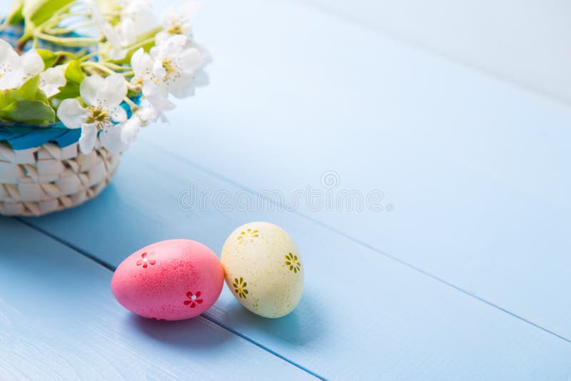 Deux ont peint les oeufs de pâques roses et jaunes près du panier avec la branche fleurissante de ressort blanc sur le fond bleu- photographie stock libre de droits Deux ont peint les oeufs de pâques roses et jaunes près du panier avec la branche fleurissante de ressort blanc sur le fond bleu- photographie stock libre de droits
