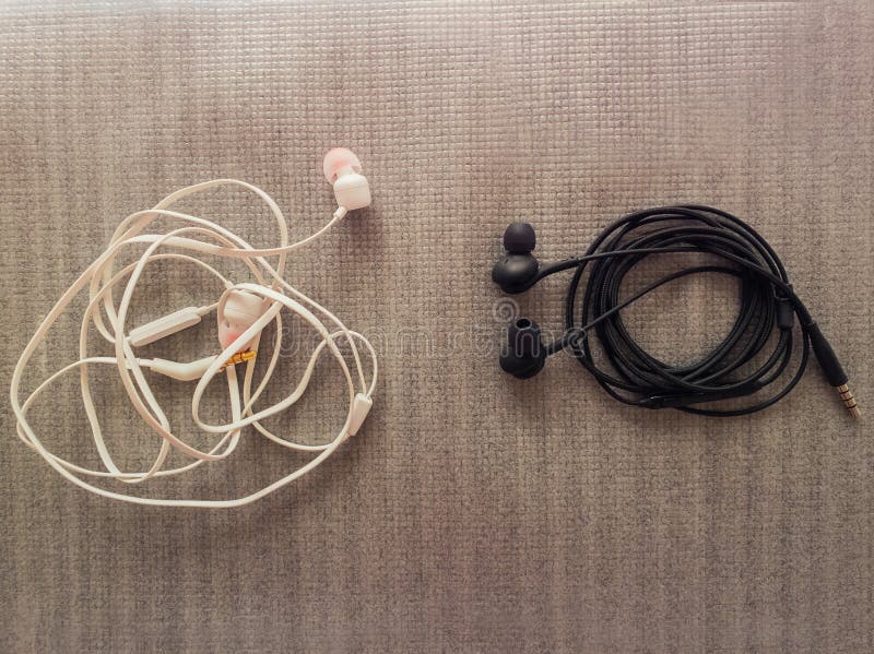 Deux paires d'écouteurs de câble noirs et blancs, pour l'écoute de musique Les différentes manières d'enveloppe, une est embrouil images stock Deux paires d'écouteurs de câble noirs et blancs, pour l'écoute de musique Les différentes manières d'enveloppe, une est embrouil images stock