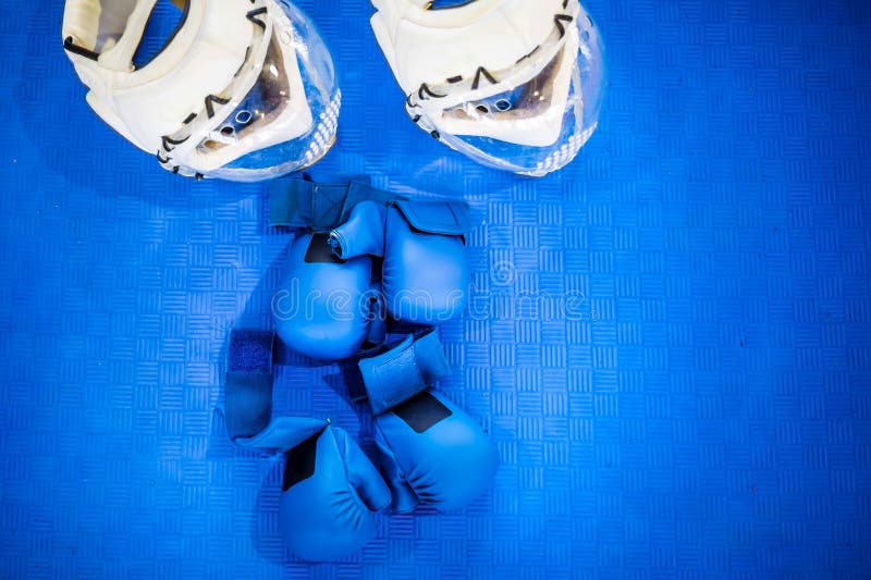 Deux paires de gants de combat bleus et de deux casques blancs avec les masques perforés en plastique clairs sur le plancher bleu photos libres de droits Deux paires de gants de combat bleus et de deux casques blancs avec les masques perforés en plastique clairs sur le plancher bleu photos libres de droits