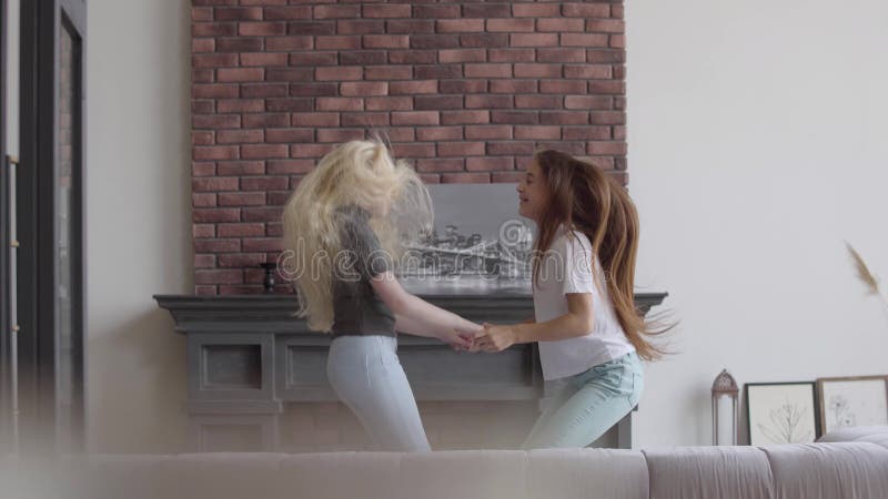 Deux petites filles avec les cheveux blonds et foncés sautant tenant des mains dans le salon Fille de brune et fille albinos avec