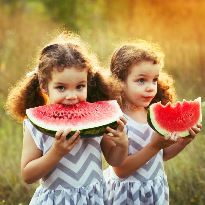 Deux petites soeurs drôles mangeant la pastèque dehors le jour chaud et ensoleillé d'été Aliment biologique sain pour de petits e photographie stock libre de droits Deux petites soeurs drôles mangeant la pastèque dehors le jour chaud et ensoleillé d'été Aliment biologique sain pour de petits e photographie stock libre de droits