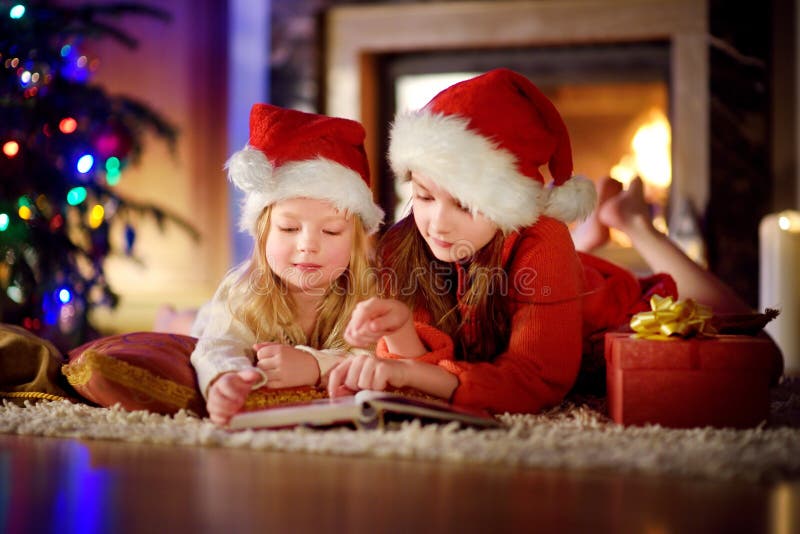Deux petites soeurs mignonnes lisant une histoire réservent ensemble sous un arbre de Noël images stock Deux petites soeurs mignonnes lisant une histoire réservent ensemble sous un arbre de Noël images stock