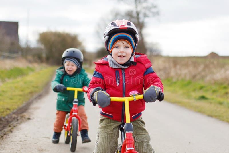 Deux petits garçons jumeaux d'enfant en bas âge ayant l'amusement sur des bicyclettes, dehors photographie stock Deux petits garçons jumeaux d'enfant en bas âge ayant l'amusement sur des bicyclettes, dehors photographie stock