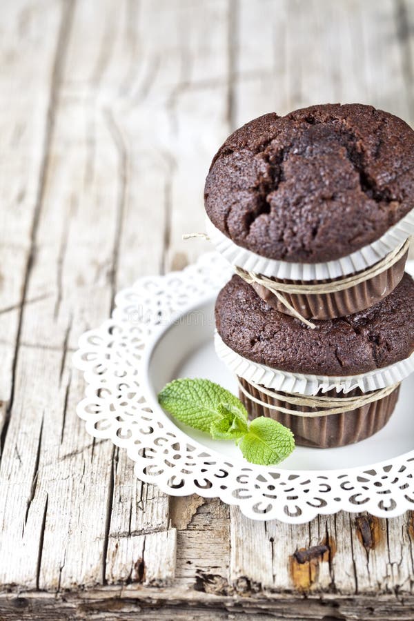 Deux petits pains fonc?s frais de chocolat avec les feuilles en bon ?tat du plat blanc sur la table en bois rustique photo stock Deux petits pains fonc?s frais de chocolat avec les feuilles en bon ?tat du plat blanc sur la table en bois rustique photo stock