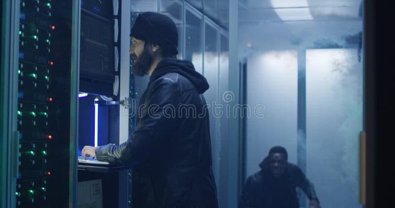 Medium, slow motion shot of a two hackers finishing hack and escaping a spark and smoke-filled corporate data center. Medium, slow motion shot of a two hackers finishing hack and escaping a spark and smoke-filled corporate data center
