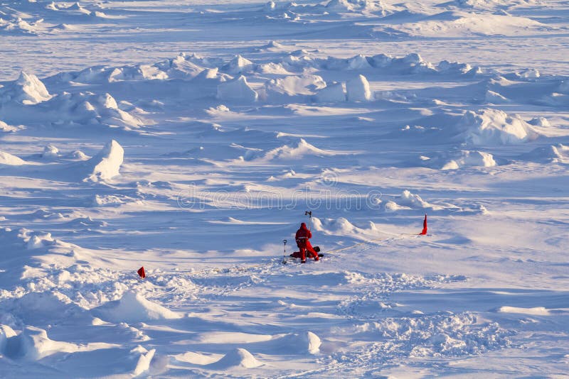 Two polar scientists in red polar clothing working on ice cores over an ice floe. Two polar scientists in red polar clothing working on ice cores over an ice floe