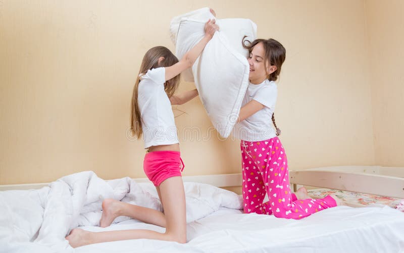 Deux soeurs dans des pyjamas combattant avec des oreillers sur le lit photo stock Deux soeurs dans des pyjamas combattant avec des oreillers sur le lit photo stock