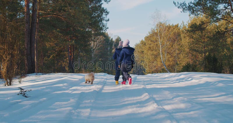 Deux soeurs marchent avec un petit chien dans une forêt d'hiver