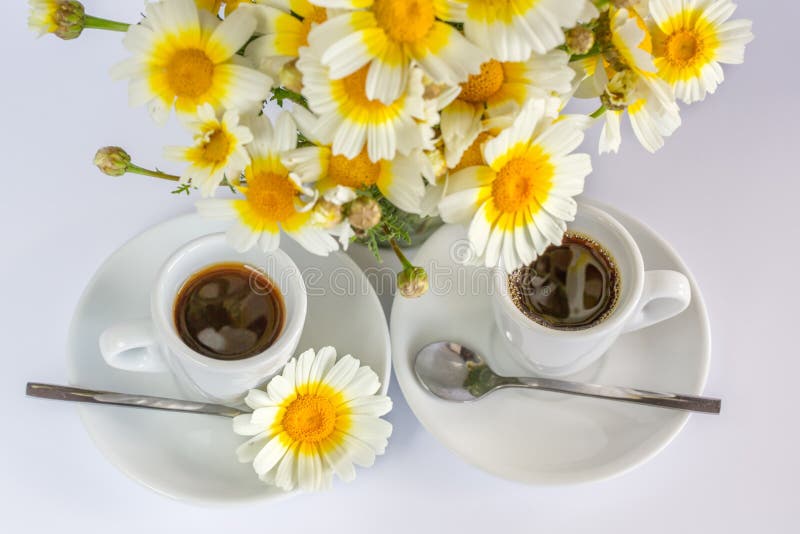 Two cups of coffee and a bouquet of camomiles on a white background. Two cups of coffee and a bouquet of camomiles on a white background