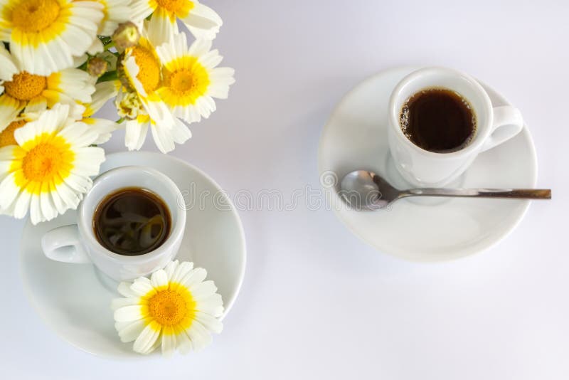 Two cups of coffee and a bouquet of camomiles on a white background. Two cups of coffee and a bouquet of camomiles on a white background