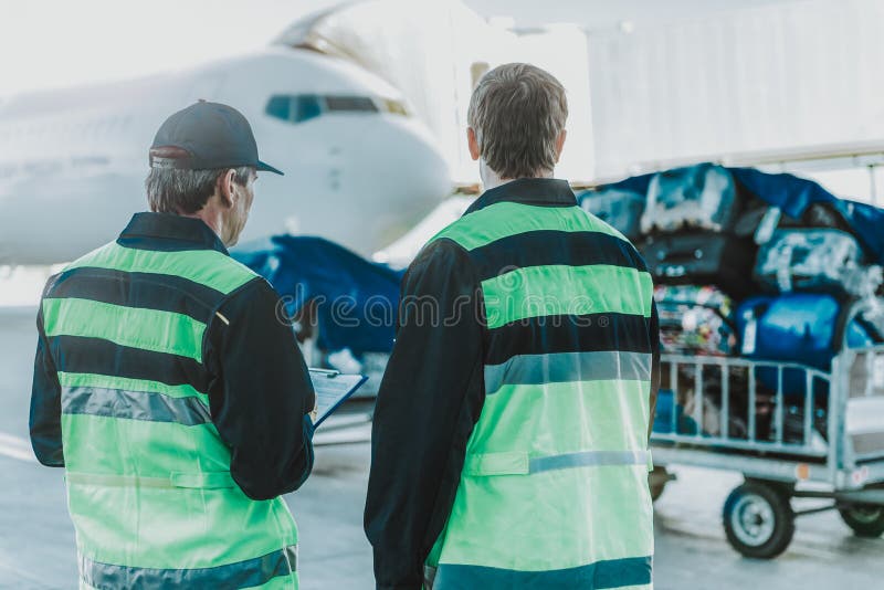 Deux travailleurs dans l'uniforme regardant le bagage image libre de droits