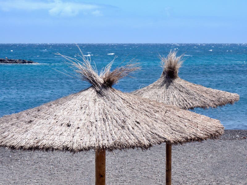 Devant l'Océan Atlantique bleu-foncé, deux parasols d'herbe tubulaire se tiennent prêt l'eau photos libres de droits Devant l'Océan Atlantique bleu-foncé, deux parasols d'herbe tubulaire se tiennent prêt l'eau photos libres de droits