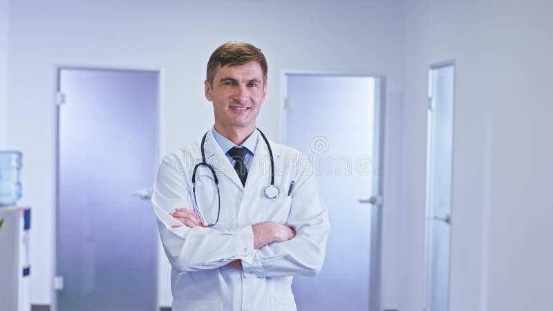 Devant le portrait de caméra d'un homme de médecin dans le couloir d'hôpital donnant directement à la caméra ayez le franchissemen