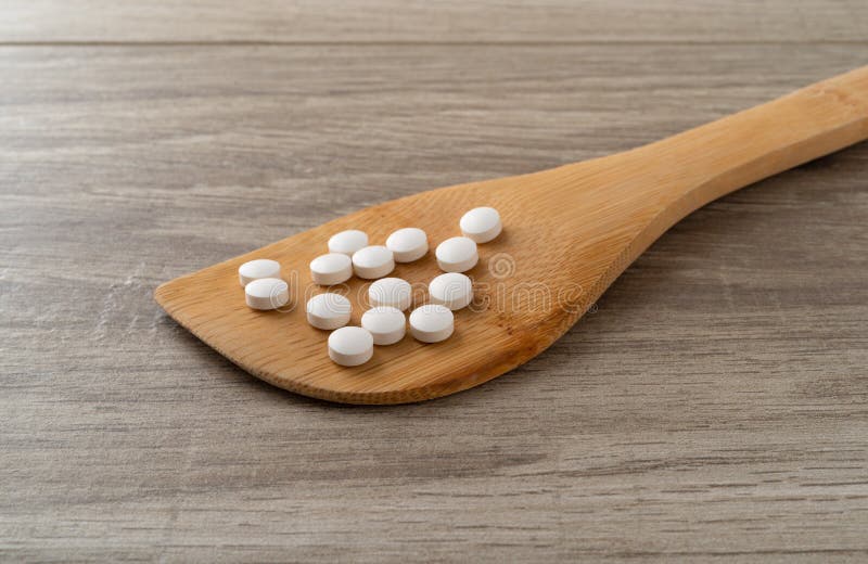 DHEA pills on a wood spoon atop a table side view royalty free stock image DHEA pills on a wood spoon atop a table side view royalty free stock image