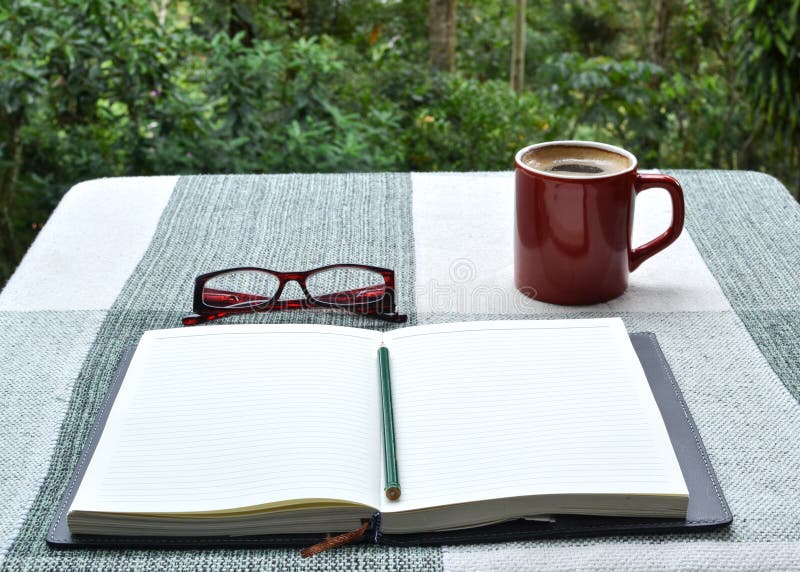 Journal, pencil, readers, and cup of coffee on table, in a tropical setting. Journal, pencil, readers, and cup of coffee on table, in a tropical setting