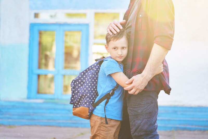 Di nuovo al banco Abbraccio felice del figlio e del padre davanti alla scuola elementare Il genitore prende il bambino alla scuol fotografia stock Di nuovo al banco Abbraccio felice del figlio e del padre davanti alla scuola elementare Il genitore prende il bambino alla scuol fotografia stock