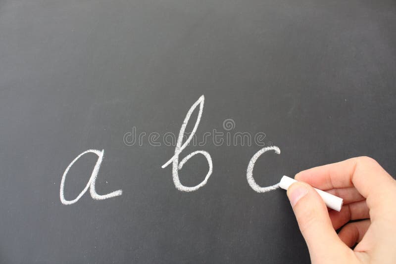 Hand holding piece of chalk, writing the alphabet on a blackboard. Hand holding piece of chalk, writing the alphabet on a blackboard