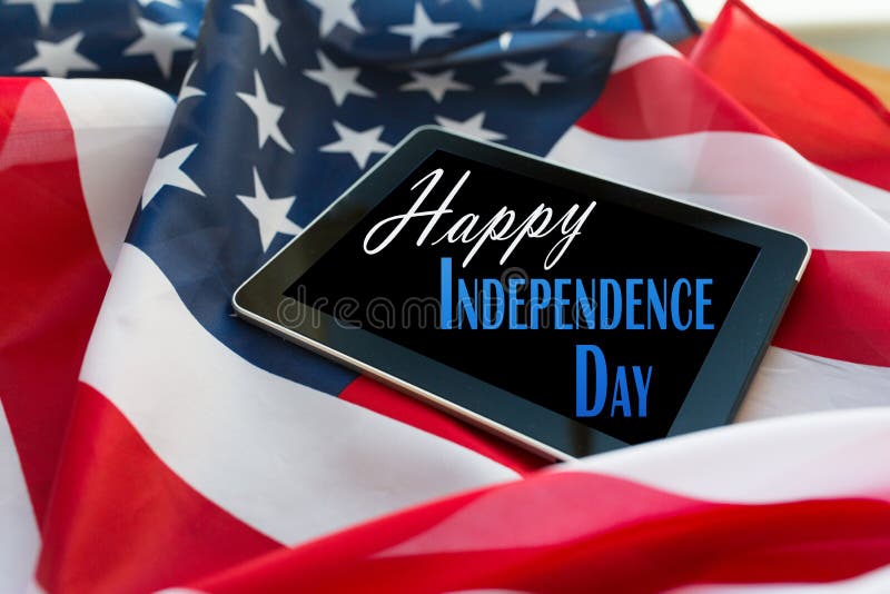Technology, memorial day, patriotism and nationalism concept - happy independence day words on tablet pc computer screen on american flag. Technology, memorial day, patriotism and nationalism concept - happy independence day words on tablet pc computer screen on american flag
