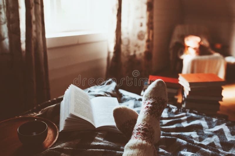 Cozy winter day at home with cup of hot tea, book and warm socks. Spending weekend in bed, seasonal holidays and hygge concept. Cozy winter day at home with cup of hot tea, book and warm socks. Spending weekend in bed, seasonal holidays and hygge concept